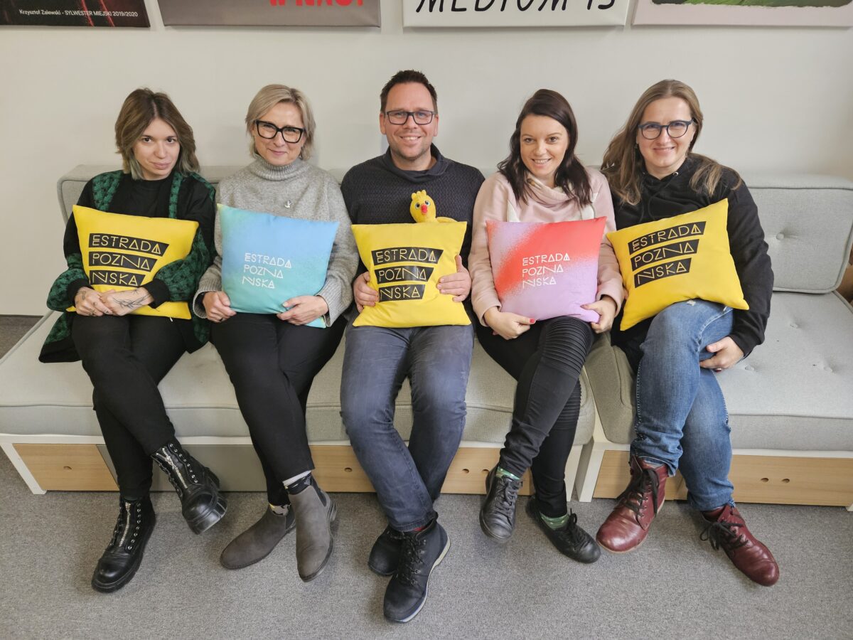 Jury konkursu siedzące na ławce. Osoby trzymają poduszki z napisem Estrada Poznańska.