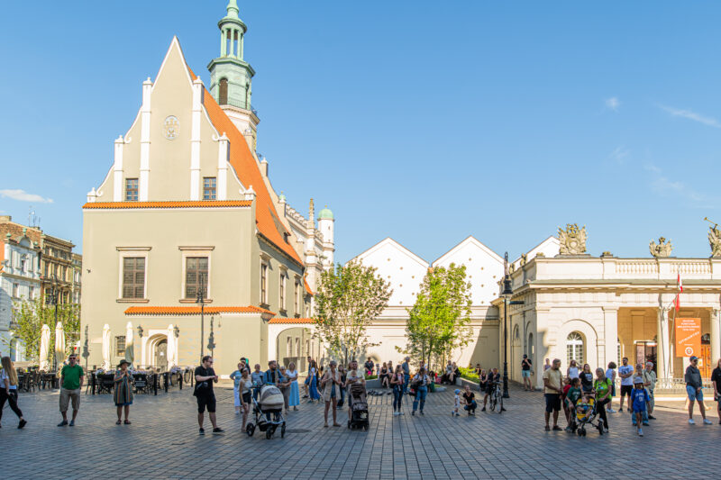 Słoneczna panorama Starego Rynku w Poznaniu oraz spacerowicze.