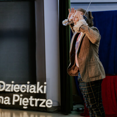 Aktor na scenie, widać ledon z napisem "Dzieciaki na Piętrze"