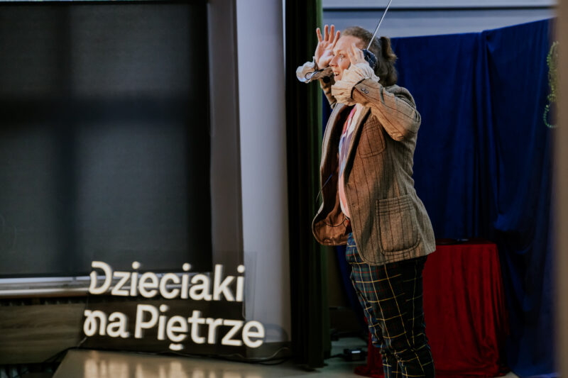 Aktor na scenie, widać ledon z napisem "Dzieciaki na Piętrze"