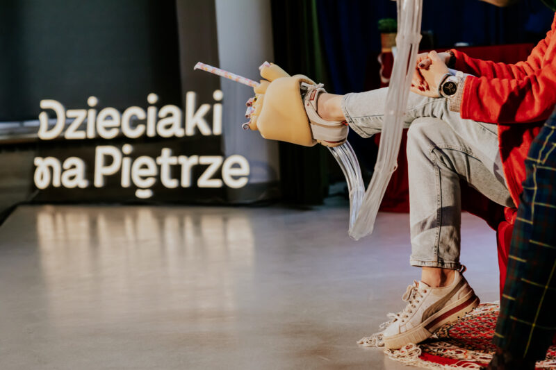 Osoba w zabawnym kostiumie na scenie, w tle napis "Dzieciaki na Piętrze"